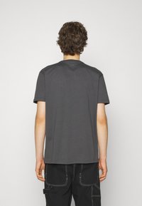 T-shirt en coton gris avec un col rond et des manches courtes, présenté de dos, avec une coupe décontractée et des détails de couture subtils.