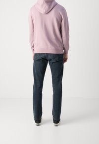 Jasnoróżowa bluza z kapturem o luźnym kroju, zestawiona z ciemnoniebieskimi dżinsami. Materiał o fakturze, minimalne szwy i klasyczny design denimu.