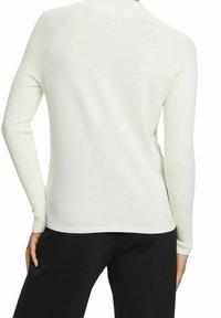 Pull blanc côtelé avec manches longues et col montant. Texture lisse et coupe ajustée. L'ourlet se termine à la taille, assorti à un pantalon noir.