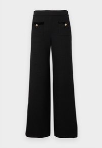 Pantalon noir à jambes larges en tissu texturé, avec deux poches avant bordées de velours et détails de boutons dorés.