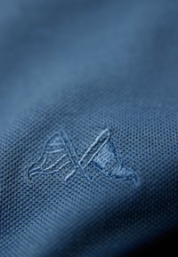 Niebieska teksturowana tkanina z tłoczonym wzorem logo wszytym w materiał, z wzorami tworzącymi subtelny połysk.