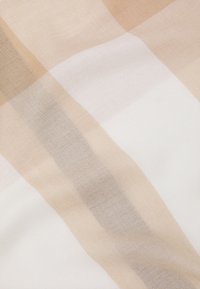 Tissu à carreaux beige et blanc avec une texture douce, présentant des rayures irrégulières. Palette de couleurs claire et neutre avec des nuances subtiles.