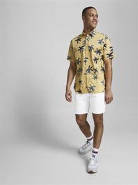 Korte mouwen gele shirt met blauwe palmbomenprint, gecombineerd met witte shorts, witte sneakers en gestreepte sokken.
