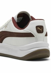Białe skórzane sneakersy z bordowym paskiem akcentującym, teksturowaną wstawką, wyściełanym kołnierzem i gumową podeszwą. Zawierają złote logo na pięcie.