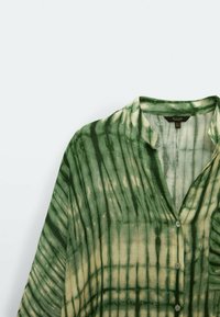Camicia tie-dye verde e crema con colletto, chiusura a bottoni e maniche lunghe. Il tessuto sembra leggero con una consistenza morbida e un motivo sottile.
