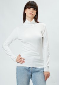 Weißer Rollkragenpullover aus weichem Stoff, mit langen Ärmeln und geripptem Saum, kombiniert mit hellblauen Jeans.