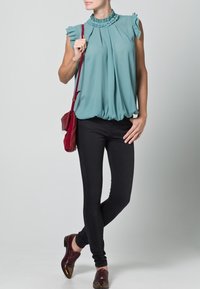 Blusa senza maniche color teal con scollo arricciato, design plissè e orlo elastico abbinata a jeans skinny neri e borsa a tracolla bordeaux.