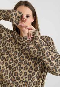 Maglione leopardato beige con macchie marroni e nere. Presenta polsini a coste e un ampio scollo, realizzato in materiale morbido e testurizzato.