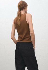 Top marrón sin mangas con un diseño ajustado, combinado con unos pantalones vaqueros de denim oscuro de cintura alta. Tela texturizada con detalles de costura visibles.