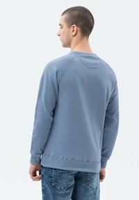 Blå sweatshirt med ribbad textur, rund halsringning och raglanärmar. Buren tillsammans med denimjeans, vilket ger en avslappnad och bekväm passform.