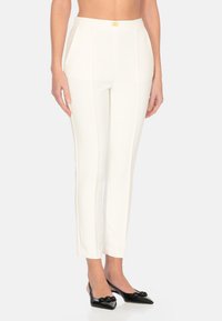 Pantaloni bianchi su misura con una texture liscia, caratterizzati da una vestibilità slim e un dettaglio in metallo dorato in vita. Abbinati a scarpe nere a punta.
