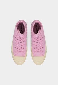 Ζευγάρι ροζ ψηλά παπούτσια Converse με υφή υφάσματος και μπεζ λαστιχένιες μύτες σε λευκό φόντο.
