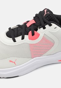 Lys grå treningssko i mesh og lærmaterialer, med svarte lisser, rosa detaljer og teksturert mønster på siden.