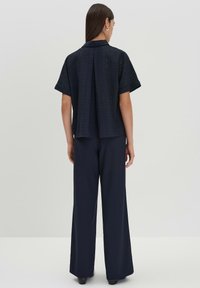 Blusa nera a maniche corte con texture, abbinata a pantaloni larghi di colore navy, caratterizzati da una vestibilità rilassata e da dettagli di design sottili.