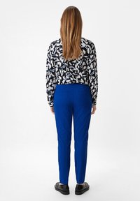 Czarna i biała bluzka w wzory zestawiona z gładkimi, niebieskimi dopasowanymi spodniami, które mają gładką fakturę i kieszenie z przodu; czarne buty.