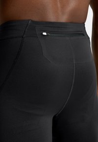 Sorte atletiske shorts med en glat tekstur; har en lynlåslomme på bagsiden og forstærkede sømme langs kanterne.