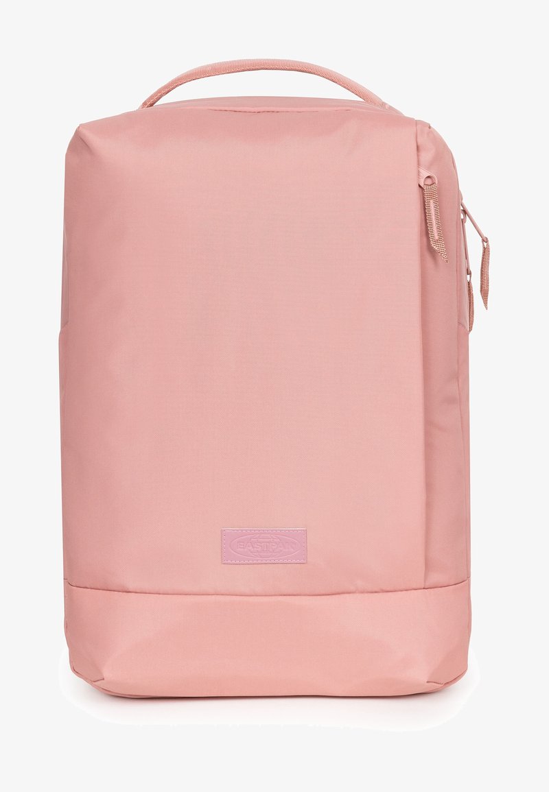 Sac à dos rectangulaire rose avec poignée supérieure, poche latérale zippée et écusson logo discret sur le panneau avant.
