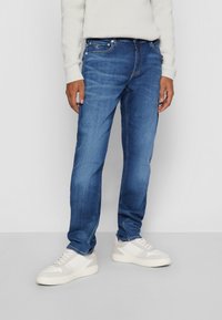 Blå denimjeans med rak passform, fem fickor och subtila sömnadsdetaljer, tillsammans med vita sneakers med en texturerad design.