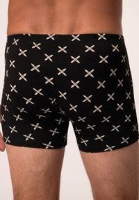 Shorts de boxeur noirs en coton avec un motif à croix blanche répétitif, dotés d'une taille élastique et d'un design ajusté.