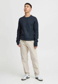 Dark navy knitted sweater with a round neckline, worn with beige pants and grey sneakers featuring black stripes. Simple design, ribbed texture.