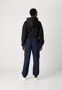 Zwarte hoodie met een relaxte pasvorm, gecombineerd met marineblauwe trainingsbroek met een elastische tailleband en boorden. Witte sneakers.