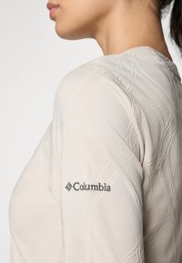 Light beige long-sleeve top with textured pattern and Columbia logo embroidered on the sleeve; fitted design with soft fabric.