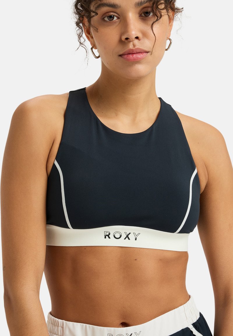 Navy sports bra with white stitching and logo. Features a high neckline and racerback design, made from a smooth, stretchy material.