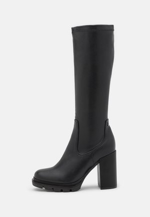 Botte en cuir noire mi-mollet avec talon bloc épais, bout arrondi et semelle crantée, vue de profil sur fond blanc.