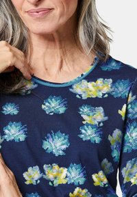 Marinefarbendes Blumenhemd mit Rundhalsausschnitt, das blau- und gelbfärbige Blumen im Aquarell-Stil zeigt und einen kontrastierenden hellblauen Saum am Kragen hat.