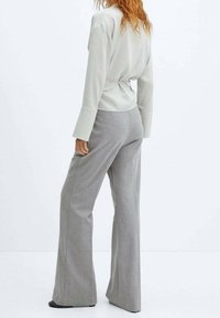 Top grigio chiaro a maniche lunghe con cintura in vita, abbinato a pantaloni larghi grigi chiari realizzati in tessuto testurizzato e dotati di tasche.