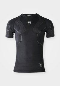 T-shirt de sport à manches courtes noir avec des panneaux texturés, des lignes courbes blanches fines, un logo de dent sur la poitrine et un badge de performance rond près de l'ourlet.