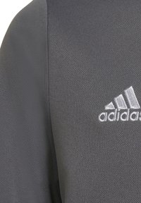 Grå atletisk sweatshirt med et tekstureret stof, der har et hvidt broderet Adidas-logo på brystet. Enkel design, ingen mønstre.
