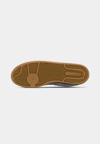 Gummisåle til joggesko med fiskebeinmønster, med en sirkulær logo-detalj. Fargen er beige med en teksturert overflate for grep.