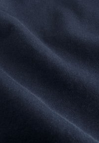 Donkerblauwe stof met een glad, gestructureerd oppervlak; zichtbare kreukels en plooien creëren diepte en dimensie in het materiaal.