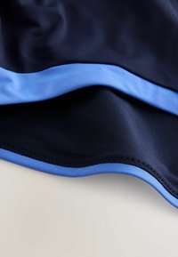 Tela de color azul marino con una textura suave, que presenta una banda de acento azul claro a lo largo del borde. El dobladillo está cuidadosamente cosido.