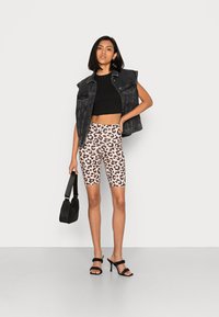Top cropped preto, colete de denim, calções de ciclismo com padrão de leopardo e sandálias de salto alto pretas, segurando uma pequena bolsa preta.