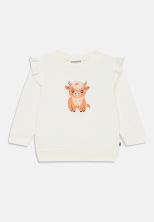 Sweatshirt de couleur crème à manches longues, avec des accents de volants sur les épaules et un graphique de vache en cartoon orange et marron à l'avant.