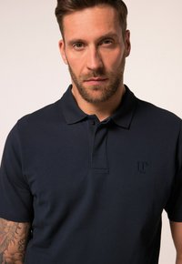 Námořnická modrá polo košile s krátkými rukávy, límečkem a nenápadným logem na hrudi. Vyrobena z texturované látky. Nabízí klasický střih.