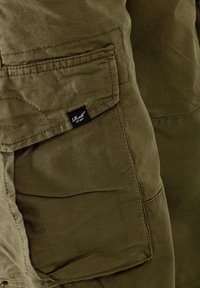 Olivgrüne Cargo-Hosen aus einem strukturierten Stoff, mit einer Seitentasche und einem kleinen schwarzen Markenetikett, das an der Naht festgenäht ist.