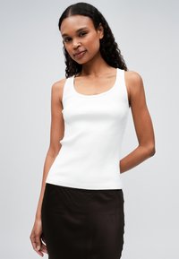 Witte geribde tanktop met een ronde halslijn en brede schouderbanden, gecombineerd met een gladde, donkerbruine rok. Eenvoudig ontwerp en aansluitende silhouette.