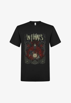 Camiseta negra de algodón con un diseño gráfico que incluye una figura roja, símbolos geométricos y el texto "IN FLAMES" en letras negritas.