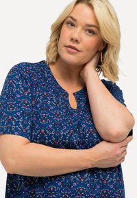 T-shirt à manches courtes en tissu bleu avec un motif floral, un détail de décolleté en trou de serrure et une texture lisse.