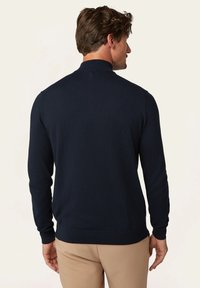 Marineblauer Strickpullover mit langen Ärmeln und hohem Kragen, der über eine strukturierte Oberfläche sowie gerippte Bündchen und Saum verfügt.