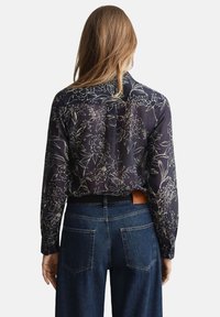 Dunkelblaue Bluse mit Blumenmuster und langen Ärmeln, mit lockerem Schnitt und Rückenpasse, kombiniert mit hoch taillierten Jeans.