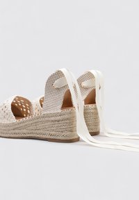 Sandalias de cuña con parte superior de yute beige trenzado, suela intermedia de yute y cintas de satén. La parte trasera tiene un diseño recortado y un forro interior suave de color marrón.