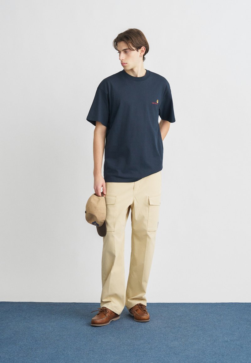 Navy cotton t-shirt with short sleeves and logo detail, paired with beige cargo pants featuring pockets, and brown lace-up shoes.