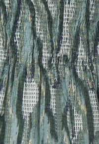 Tissu présentant un motif ondulé dans des nuances de vert et de bleu, avec des rayures texturées et des accents en grille blanche contrastante.