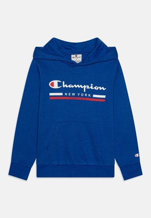 Sudadera con capucha azul de Champion con bolsillo frontal, texto del logo en blanco y rojo "Champion New York Since 1919" y pequeño emblema en la manga izquierda.