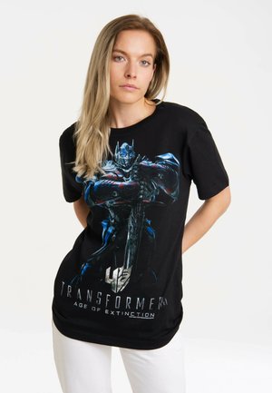 Black cotton t-shirt featuring a colorful graphic of a character holding a sword, with text "TRANSFORMERS AGE OF EXTINCTION" below.