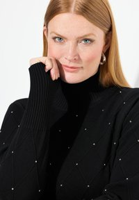 Svart stickad tröja med ribbad polokrage och diamantmönster prydd med små silverdetaljer. Mjuk textur och åtsittande design.